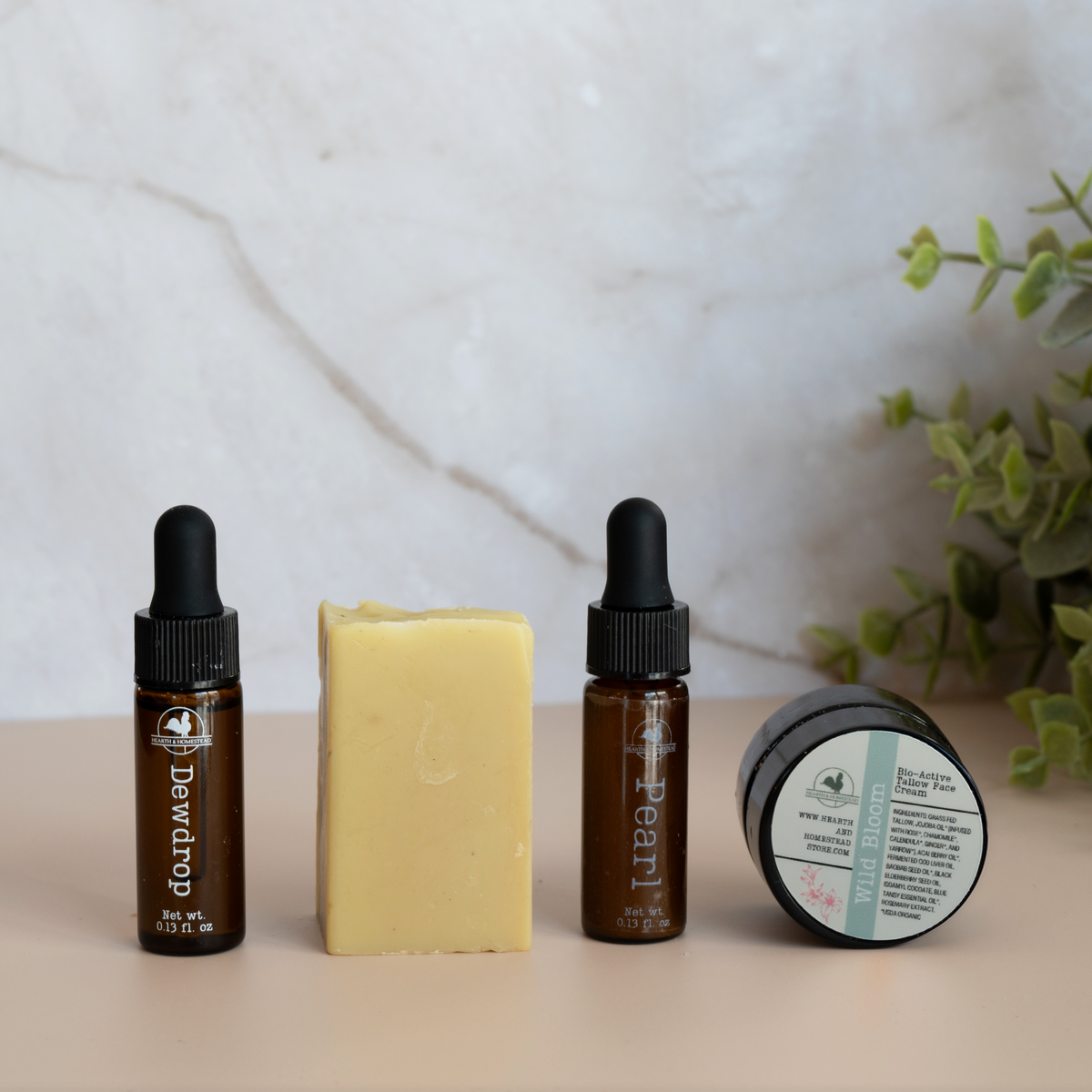 Two dropper bottles, a bar of soap, and a small container on a neutral surface with a plant in the background.