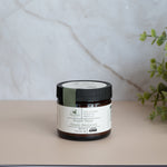 Jar of cream with a label on a light surface next to a plant