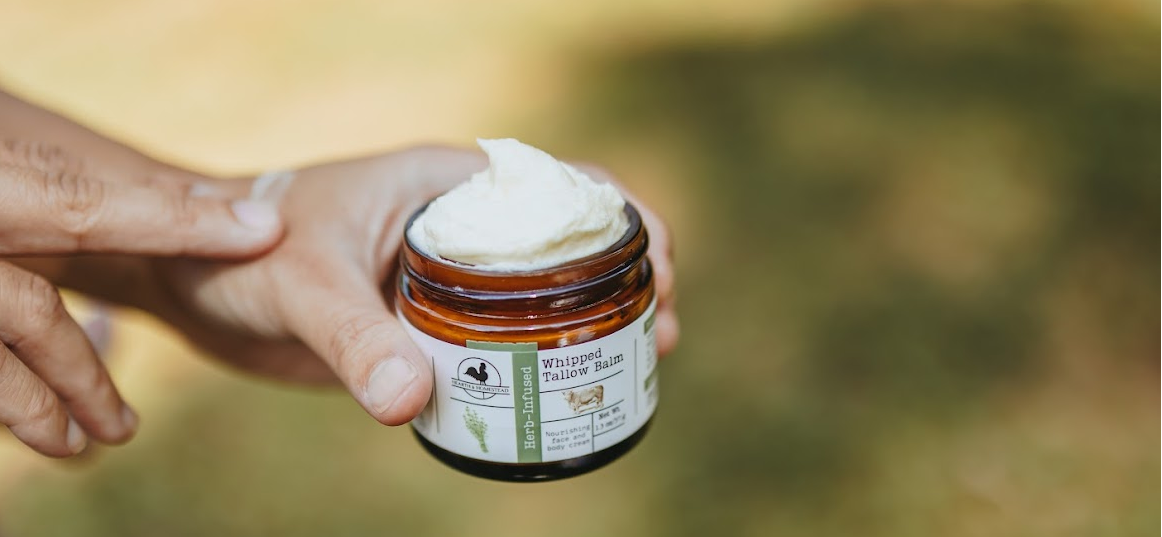 Person holding a jar of Tallow balm with a blurred natural background